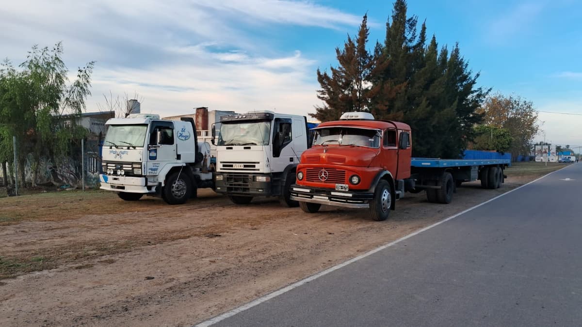 Tres camiones estacionados en fila al atardecer: un Ford Cargo, un Iveco y un Mercedes-Benz 1114 con semirremolque playo